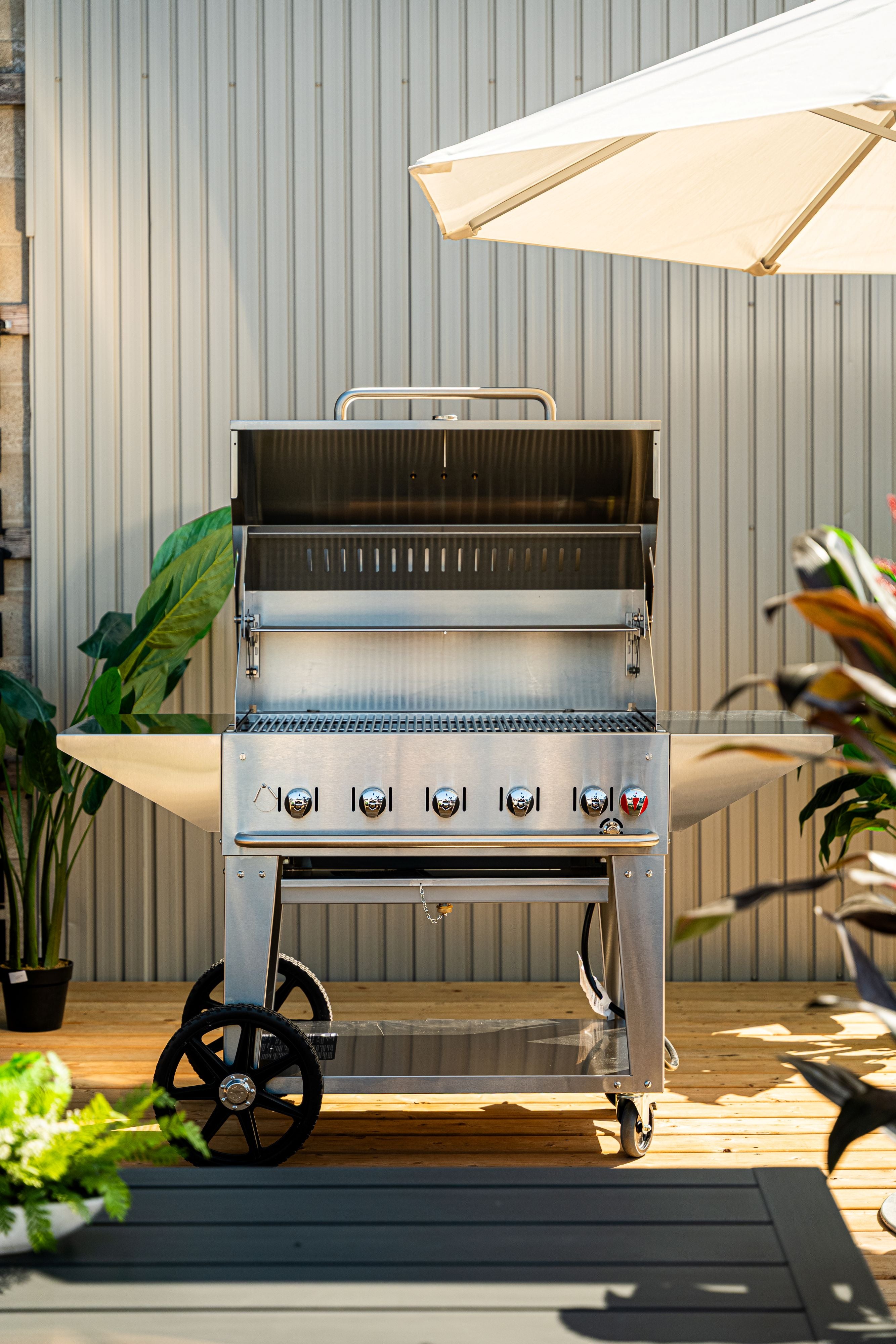 Outdoor grill on a wooden deck with plants and an umbrella in the background